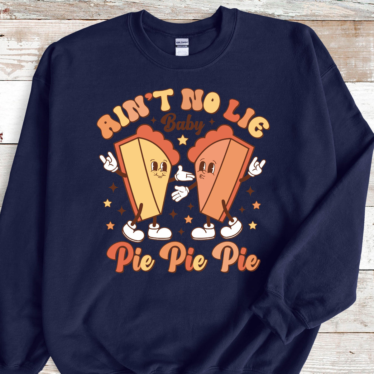 May include: A navy blue crewneck sweatshirt featuring a graphic of two anthropomorphic pie slices with arms and legs. The text reads "AIN'T NO LIE Baby" and "Pie Pie Pie" in a retro font, surrounded by small star shapes in orange and yellow tones.