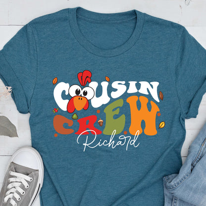 May include: A teal short-sleeve t-shirt featuring a graphic of a cartoon turkey head and the text "COUSIN CREW" in large, colorful, wavy letters. Below the text, the name "Richard" is printed in a white script font, surrounded by small leaves.