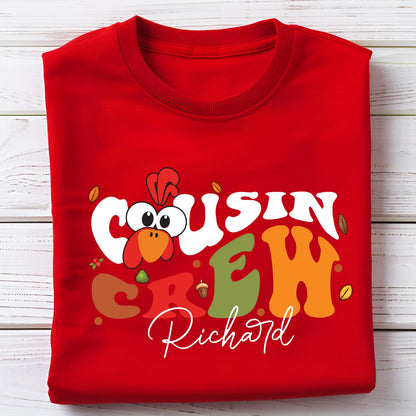 May include: A bright red crew neck t-shirt featuring a graphic print with the text "COUSIN CREW" in large, colorful, wavy letters. A cartoon turkey head replaces the letter "O" in "COUSIN". The name "Richard" is printed below in white script.
