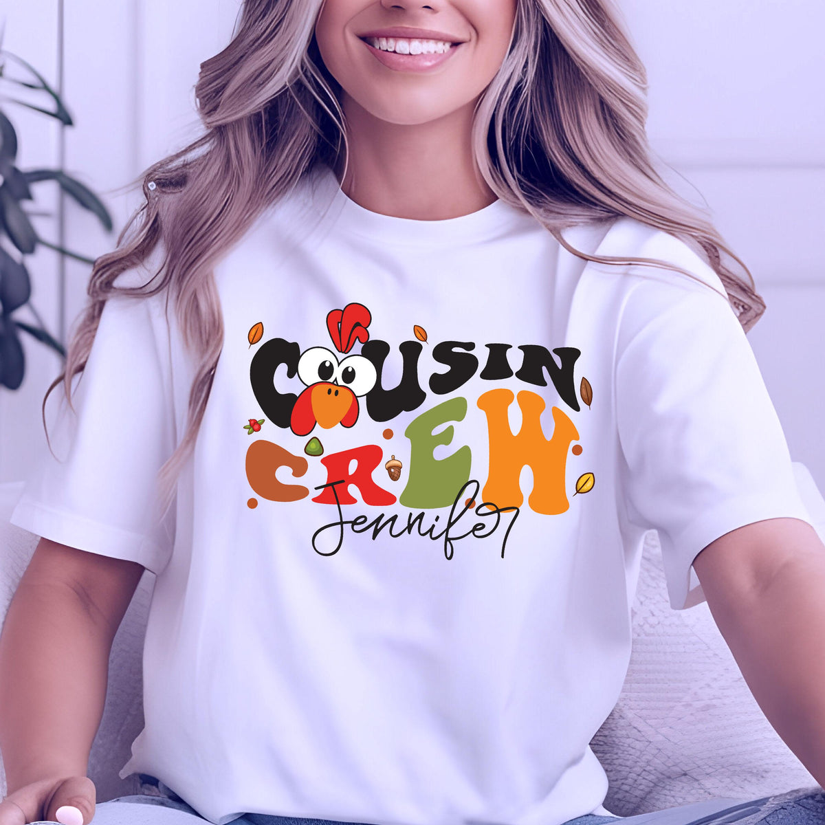 May include: A white short-sleeved t-shirt featuring a colorful graphic print with the text "COUSIN CREW" in a bold, wavy font. The design includes a cartoon turkey head, small autumn leaves, and the name "Jennifer" written in black script below.