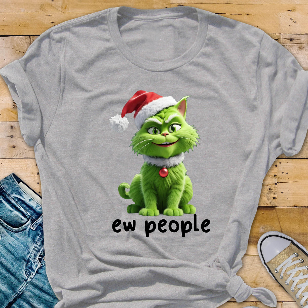 May include: A light gray short-sleeved t-shirt featuring a graphic of a green cat wearing a red and white Santa hat and a red ornament collar. Below the cat, the text "ew people" is printed in black, lowercase, sans-serif lettering.