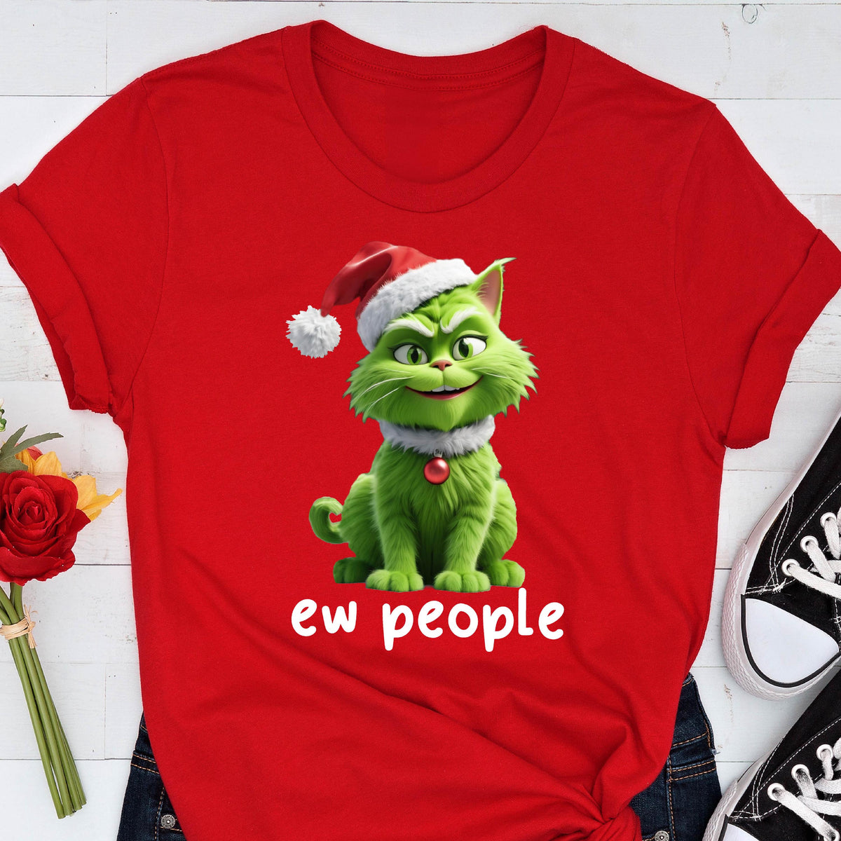 May include: A bright red short-sleeved t-shirt featuring a graphic of a green cat wearing a Santa hat and a red ornament collar. The cat has a mischievous expression, and the white text below the graphic reads "ew people" in a simple font.