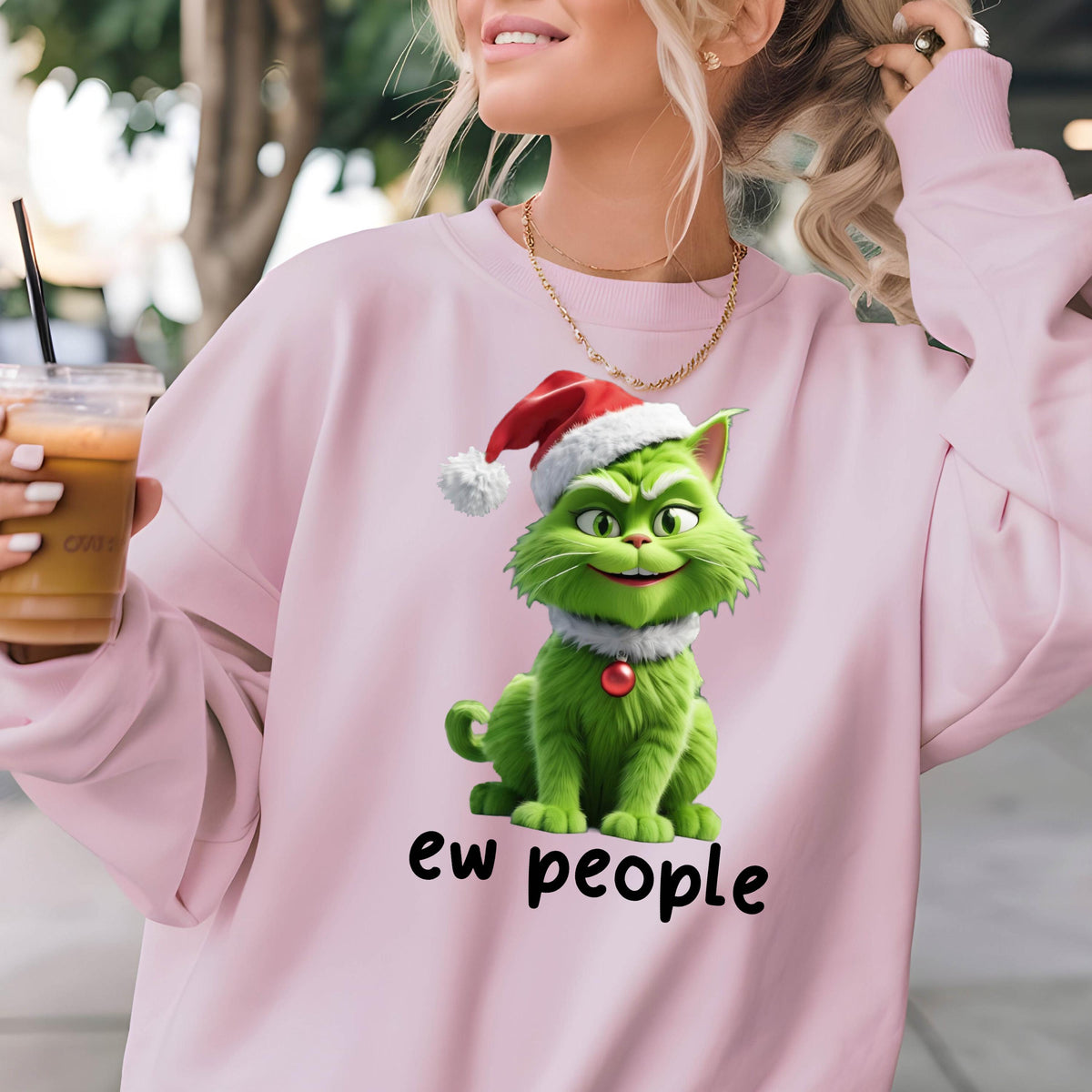 May include: A light pink sweatshirt featuring a green cartoon cat wearing a Santa hat and a red collar. The text "ew people" is printed in black below the cat. The sweatshirt has long sleeves.