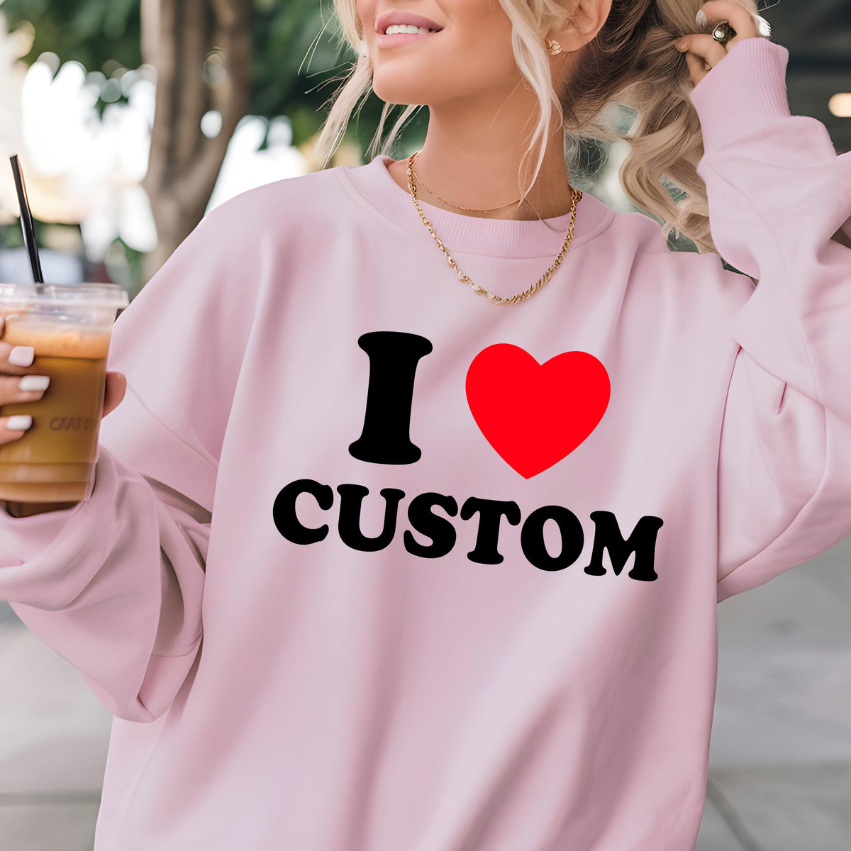 May include: A light pink sweatshirt with the text "I ♥ CUSTOM" in black and red. The sweatshirt has long sleeves and a crew neck. A gold necklace is visible.