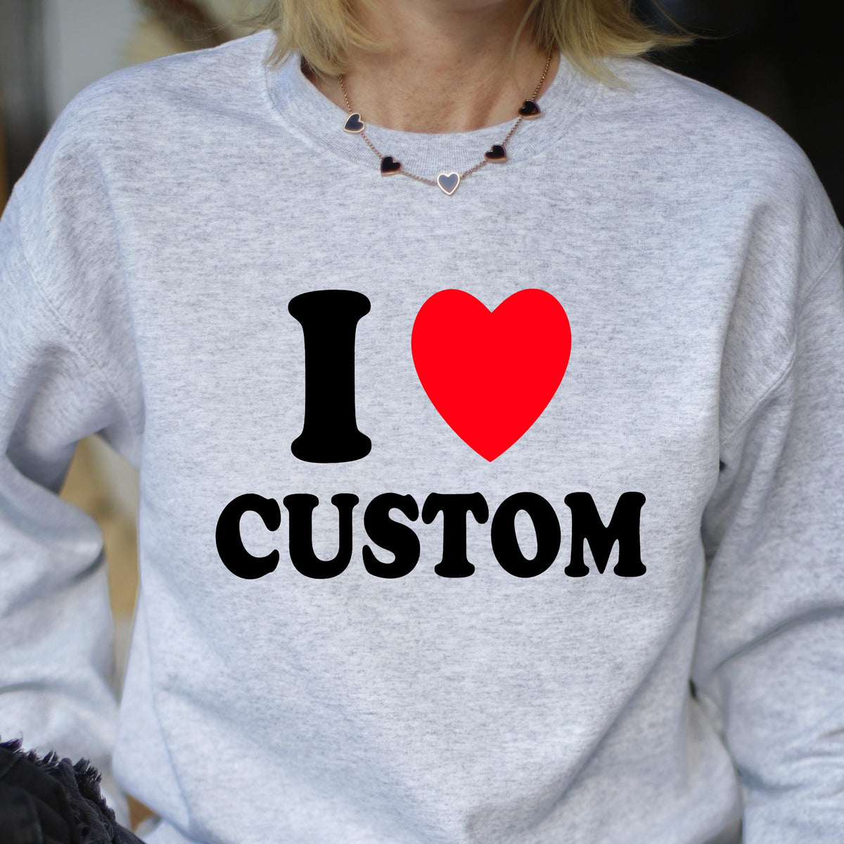 May include: A light gray sweatshirt with the text "I ♥ CUSTOM" in black and red. The "I" and "CUSTOM" are in a bold font, and the heart is a solid red color. The sweatshirt is a crew neck style.