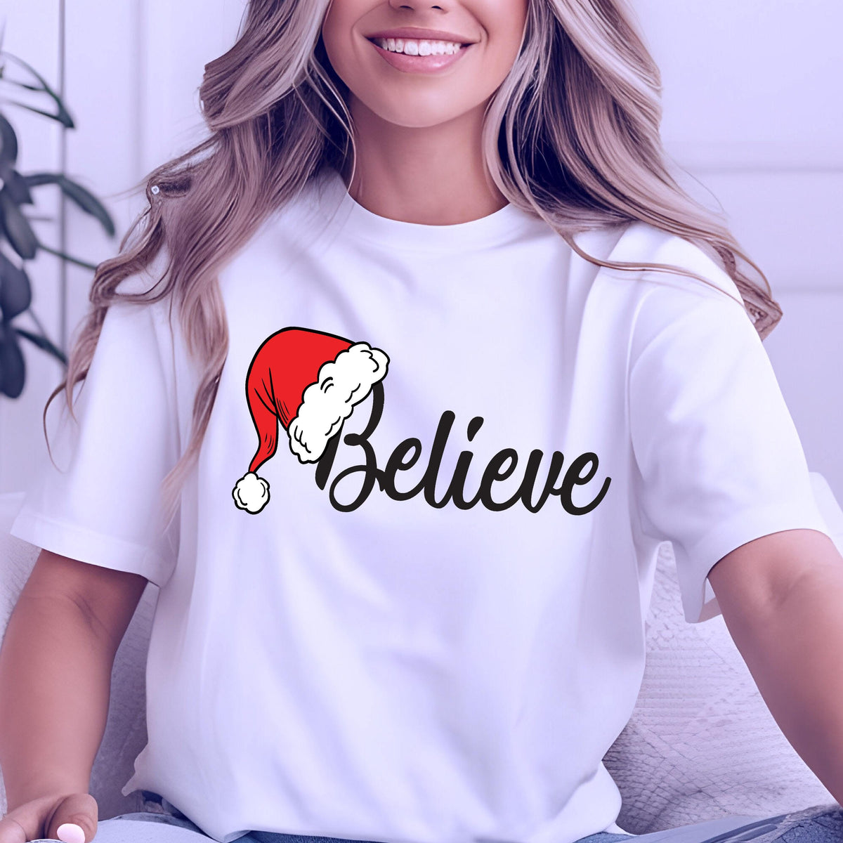 May include: A white short-sleeved t-shirt featuring a graphic print on the chest. The design includes the word Believe in a black cursive script font, with a red and white Santa Claus hat positioned over the letter B.