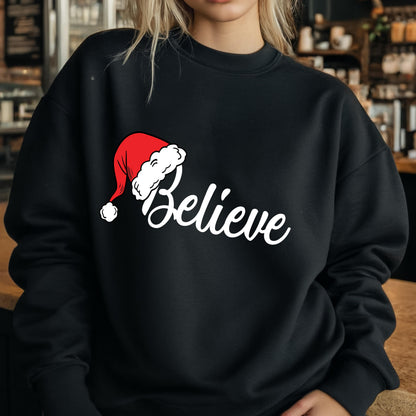 May include: A black long-sleeve crewneck sweatshirt featuring the word Believe in white cursive script. A red and white Santa hat is positioned above the letter B, replacing the dot on the letter i with the white pom-pom of the hat.