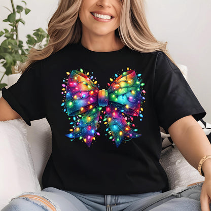 May include: Black t-shirt featuring a vibrant, colorful bow design adorned with string lights. The bow is rendered in shades of blue, green, yellow, orange, and purple, with the lights adding a festive touch. The shirt is a classic crew neck style.