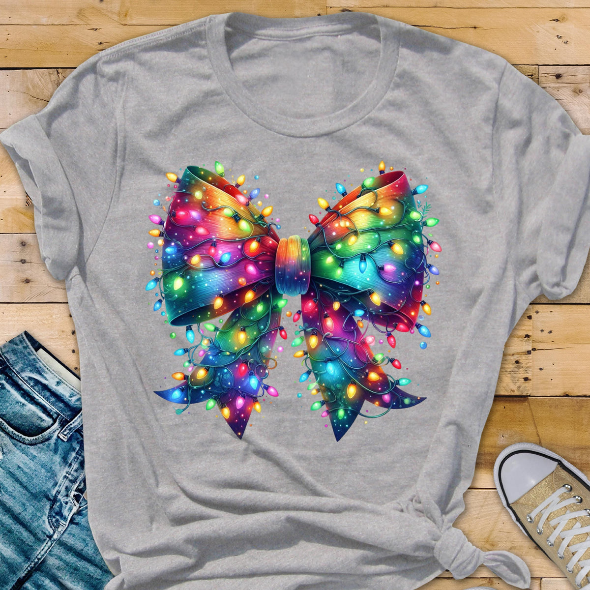 May include: A gray t-shirt featuring a colorful bow design adorned with Christmas lights. The bow is rendered in a vibrant array of colors, including red, green, blue, and yellow, with the lights adding a festive touch. The shirt is casual wear.
