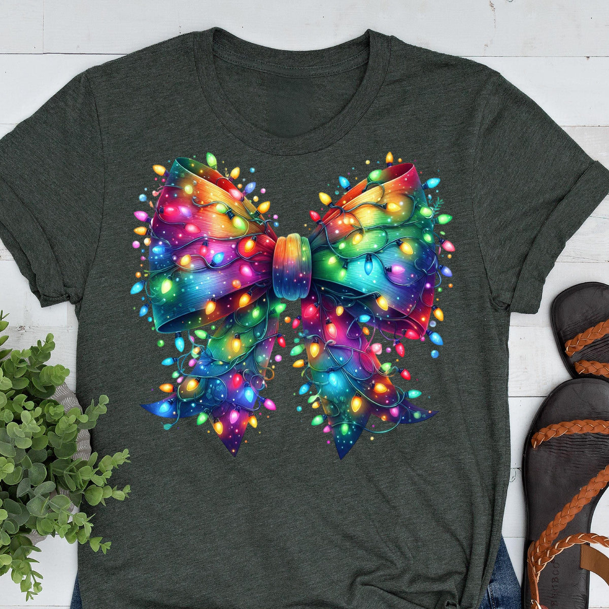 May include: Dark gray t-shirt featuring a vibrant, colorful bow design. The bow is adorned with a string of multicolored lights, creating a festive and eye-catching appearance. The design is centered on the shirt, making it a statement piece.