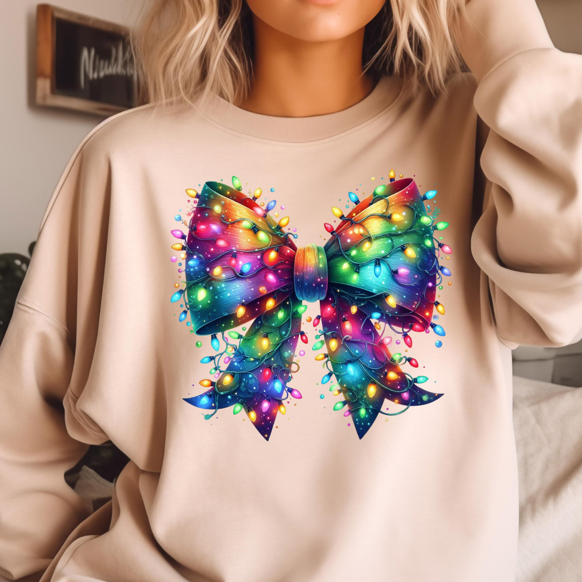 May include: A beige crewneck sweatshirt featuring a large, central graphic of a decorative bow. The bow is rendered in a vibrant, multi-colored gradient pattern and is intricately wrapped with glowing, multi-colored string Christmas lights.