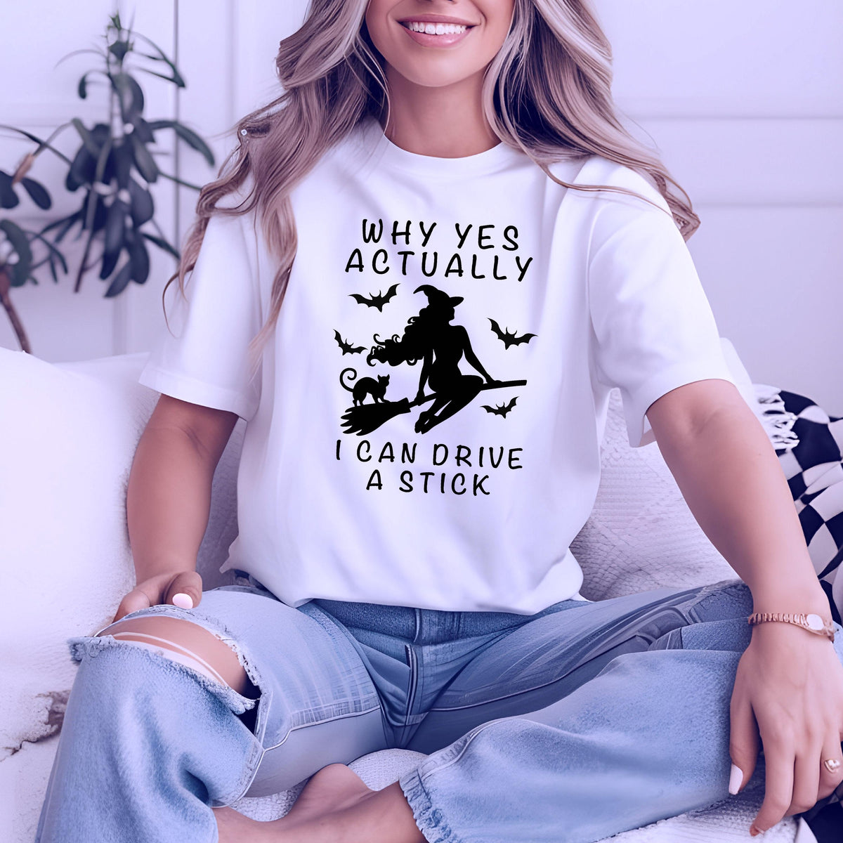 May include: White t-shirt with a black graphic of a witch on a broomstick, a black cat, and bats. The text on the shirt reads "WHY YES ACTUALLY I CAN DRIVE A STICK".