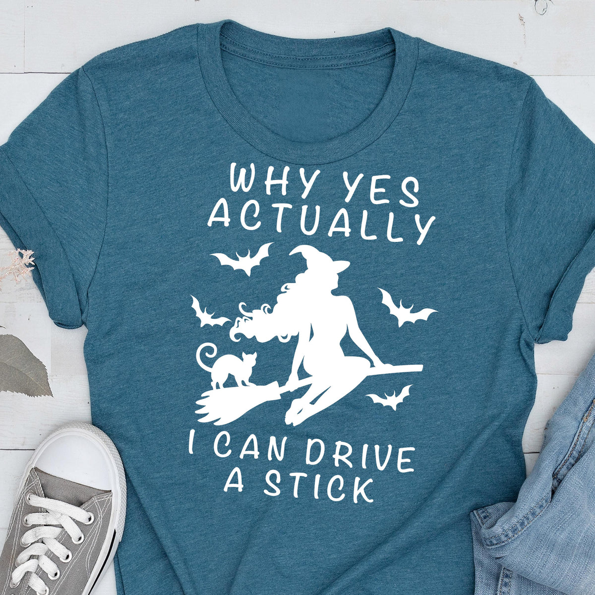 May include: Teal t-shirt with a white graphic of a witch on a broom, a black cat, and bats. The text reads "WHY YES ACTUALLY I CAN DRIVE A STICK."