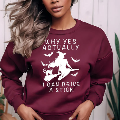 May include: A maroon long-sleeve sweatshirt featuring a white graphic of a witch riding a broomstick with a cat and bats. The text reads: WHY YES ACTUALLY I CAN DRIVE A STICK. The design is centered on the chest of the crewneck pullover garment.