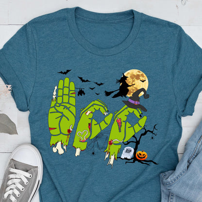 May include: A teal short-sleeve t-shirt featuring a graphic of three green zombie hands forming the letters B-O-O. The design includes a witch on a broomstick, a full moon, bats, a spider web, a tombstone with RIP text, and a jack-o'-lantern.