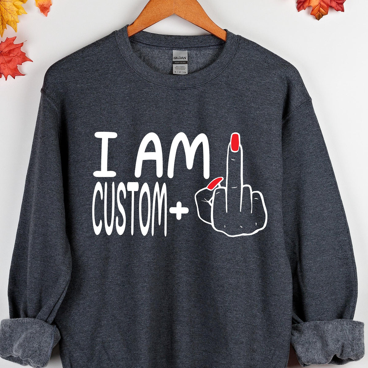 May include: A dark gray sweatshirt with the text "I AM CUSTOM+" and a white hand with red fingernails giving the middle finger.