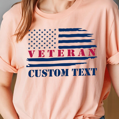 May include: Peach-colored t-shirt featuring a distressed American flag design. The flag includes blue stars, blue and red stripes, and the word "VETERAN" in red. Below the flag is the text "CUSTOM TEXT" in blue.