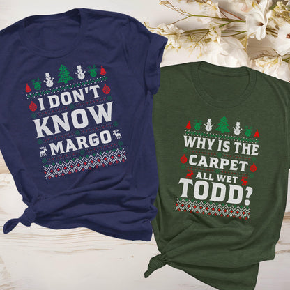 May include: Two t-shirts with holiday-themed text. One is navy blue with the text "I DON'T KNOW MARGO" and the other is green with the text "WHY IS THE CARPET ALL WET TODD?" Both shirts have a festive design.