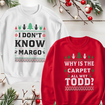 May include: Two Christmas sweaters with a festive design. The white sweater says "I don't know Margo" and the red sweater says "Why is the carpet all wet Todd?"
