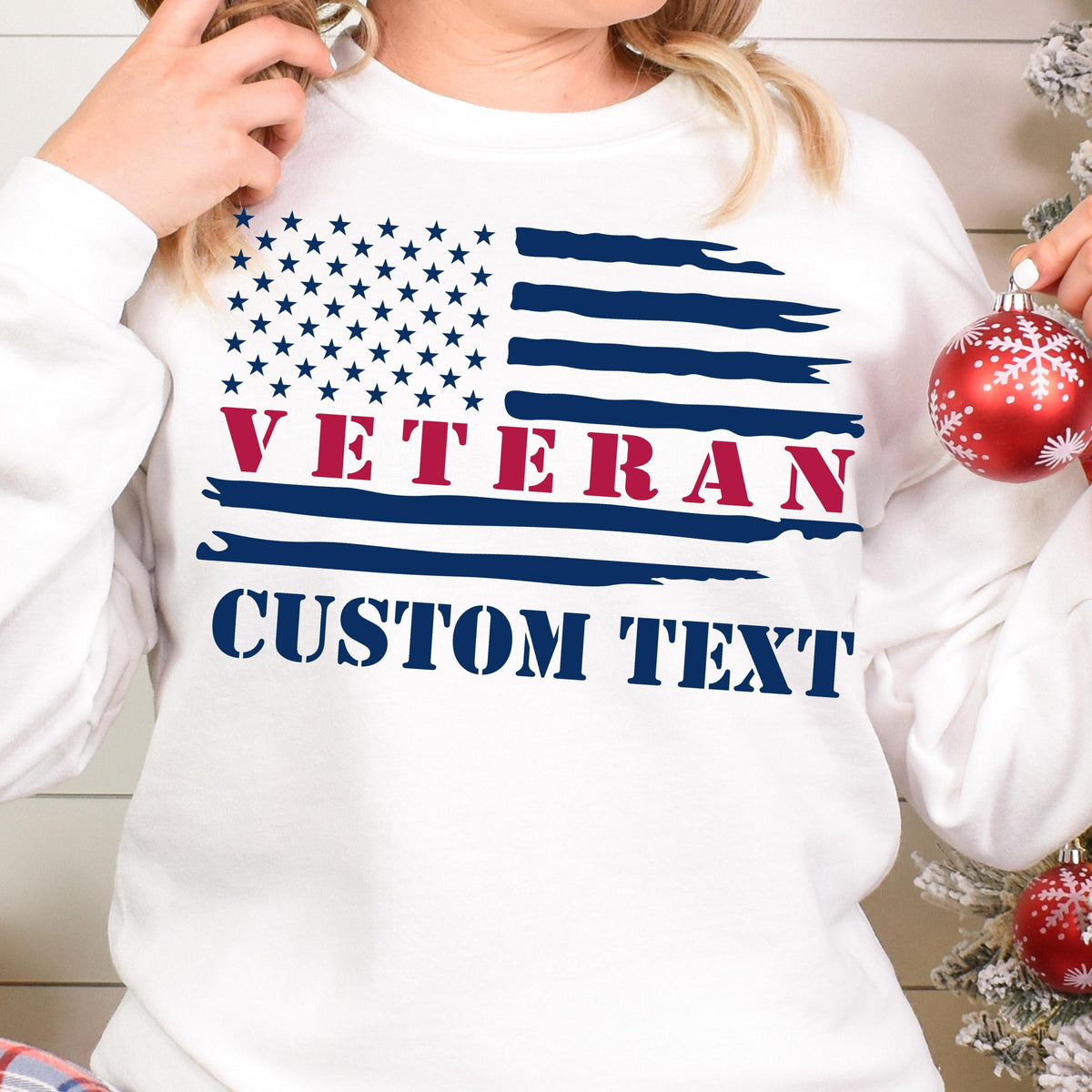 May include: White sweatshirt featuring a distressed American flag design with the word "VETERAN" in red and "CUSTOM TEXT" in navy blue. The sweatshirt has a crew neck and long sleeves.
