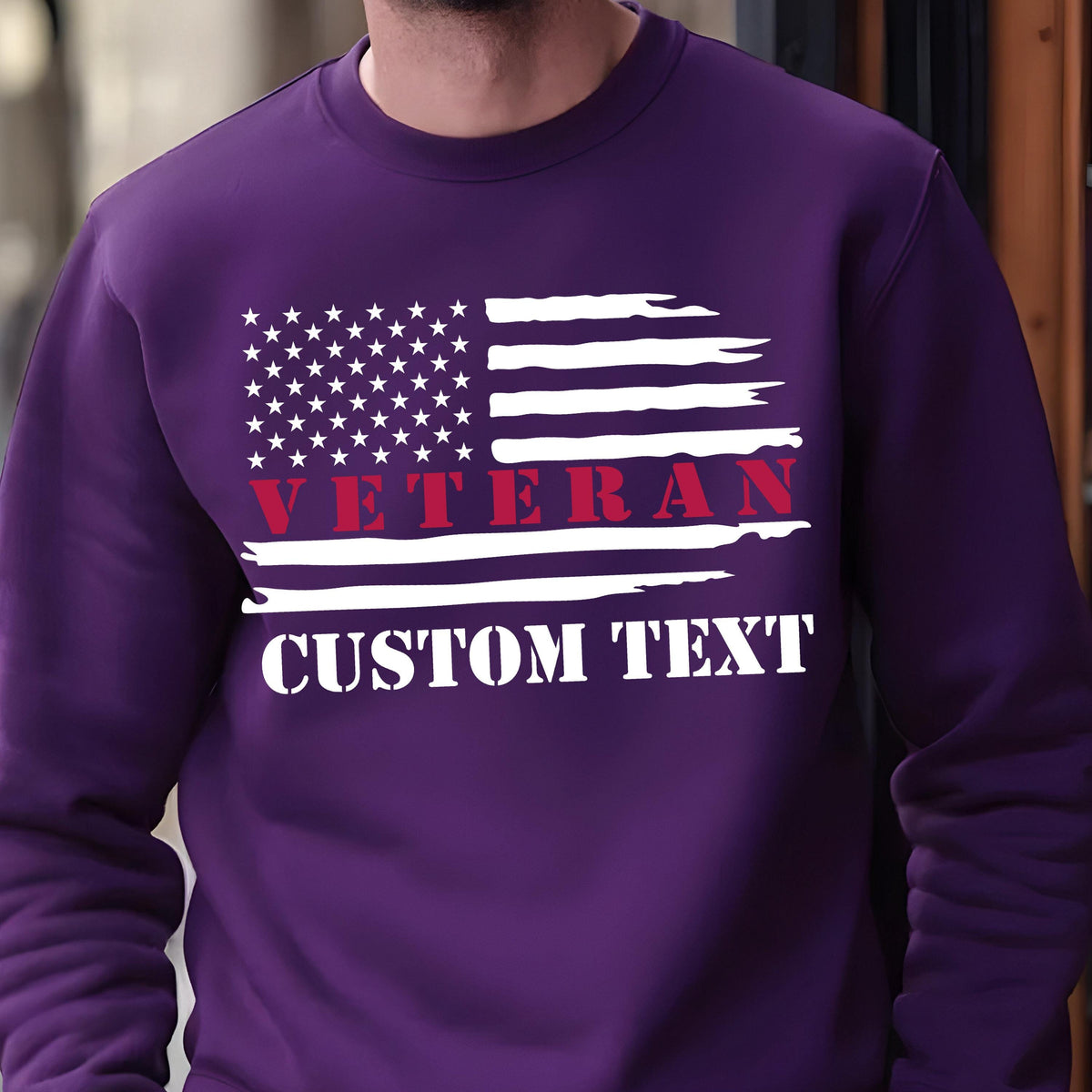 May include: A purple sweatshirt featuring a distressed American flag design. The flag includes white stars and stripes, with the word "VETERAN" in red and "CUSTOM TEXT" in white. The sweatshirt is a solid color.