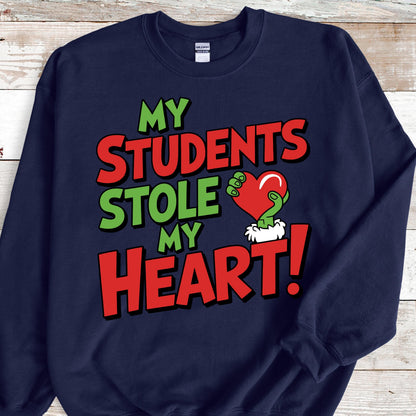 May include: Navy blue sweatshirt with the text "MY STUDENTS STOLE MY HEART!" in red and green. The design includes a green hand holding a red heart. A fun and festive design for teachers.