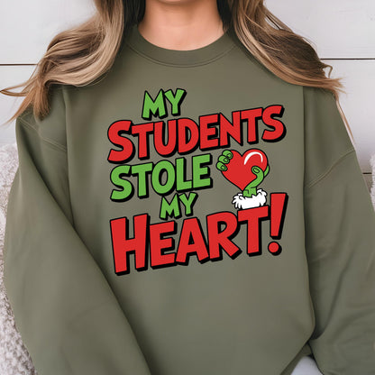 May include: Olive green sweatshirt with the text "MY STUDENTS STOLE MY HEART!" in red and green. The design includes a green hand holding a red heart. A fun and festive design for teachers.