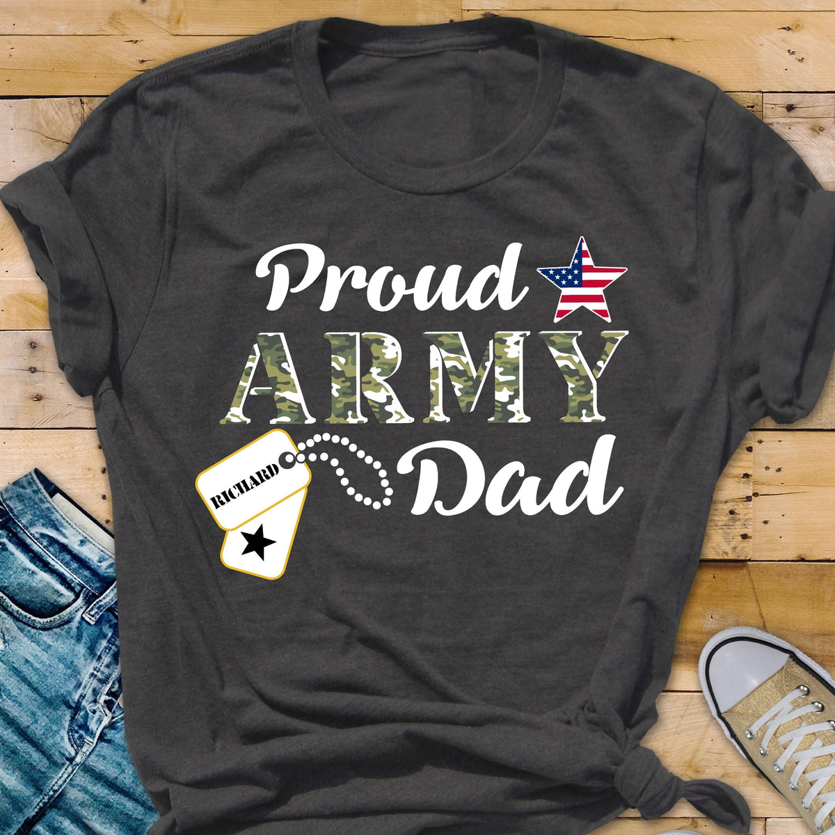 May include: Dark gray t-shirt with the words "Proud ARMY Dad" in white script and camouflage print. An American flag star graphic is above the word "Dad". A dog tag with the name "Richard" is attached.