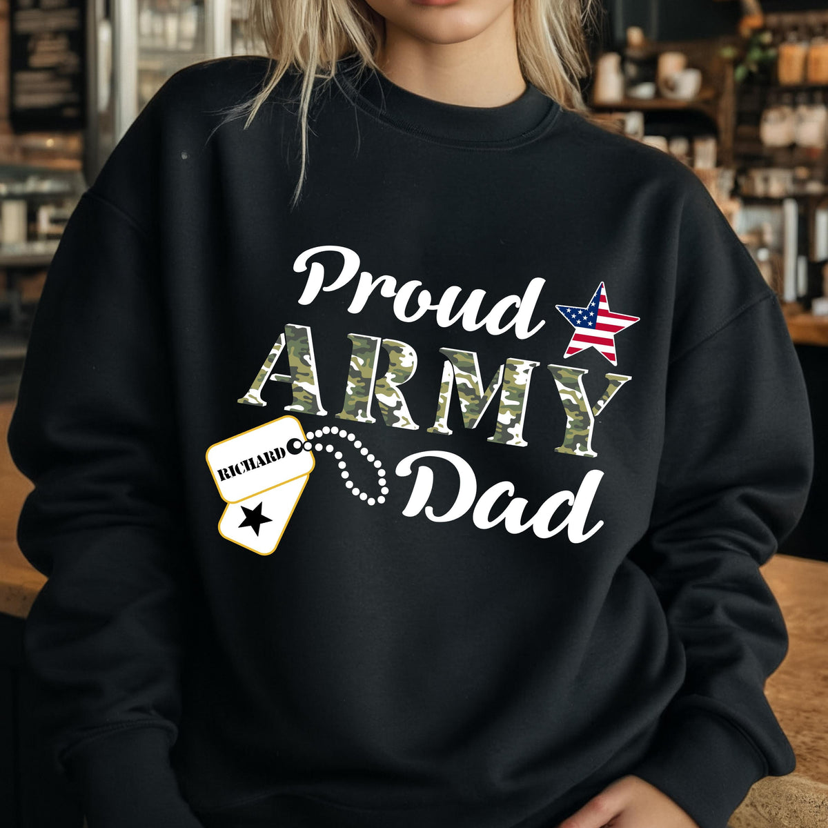 May include: Black sweatshirt with the text "Proud Army Dad" in white script. The word "ARMY" is in camouflage print. A star with the American flag design and a dog tag with the name "Richard" are also featured.