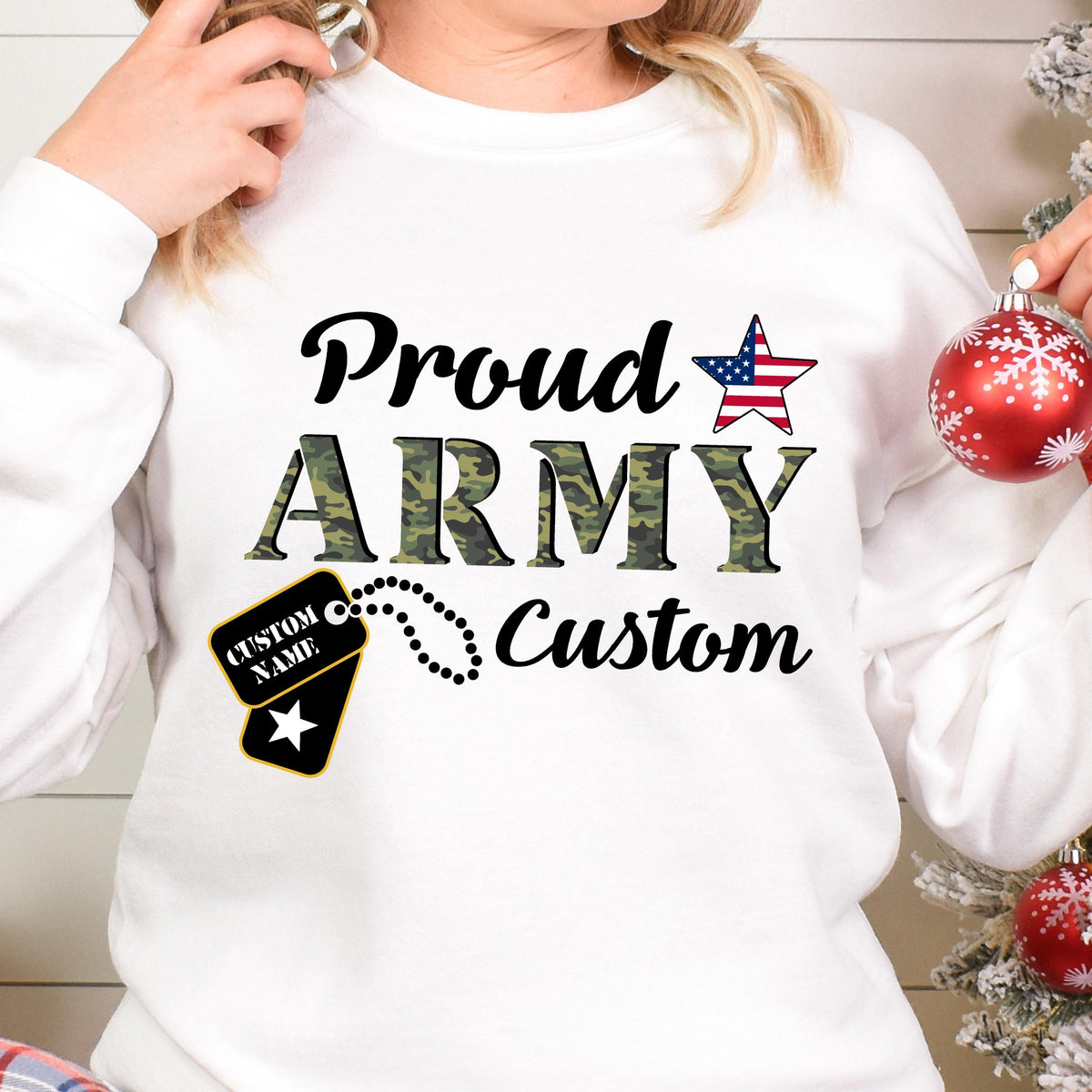 May include: White sweatshirt with the words "Proud ARMY Custom" in black and camouflage green. A star with the American flag design is above the word "ARMY". A dog tag with the words "CUSTOM NAME" is also featured.