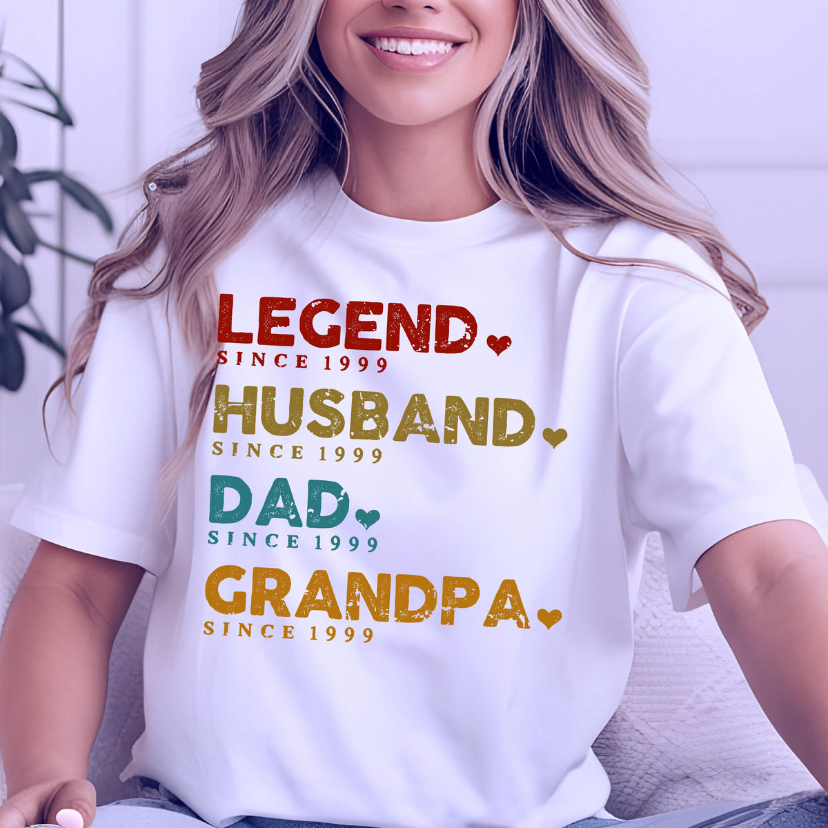 May include: White t-shirt with the words "LEGEND, HUSBAND, DAD, GRANDPA" in various colors, each followed by "SINCE 1999". The design includes small heart symbols. A casual, everyday wear tee.
