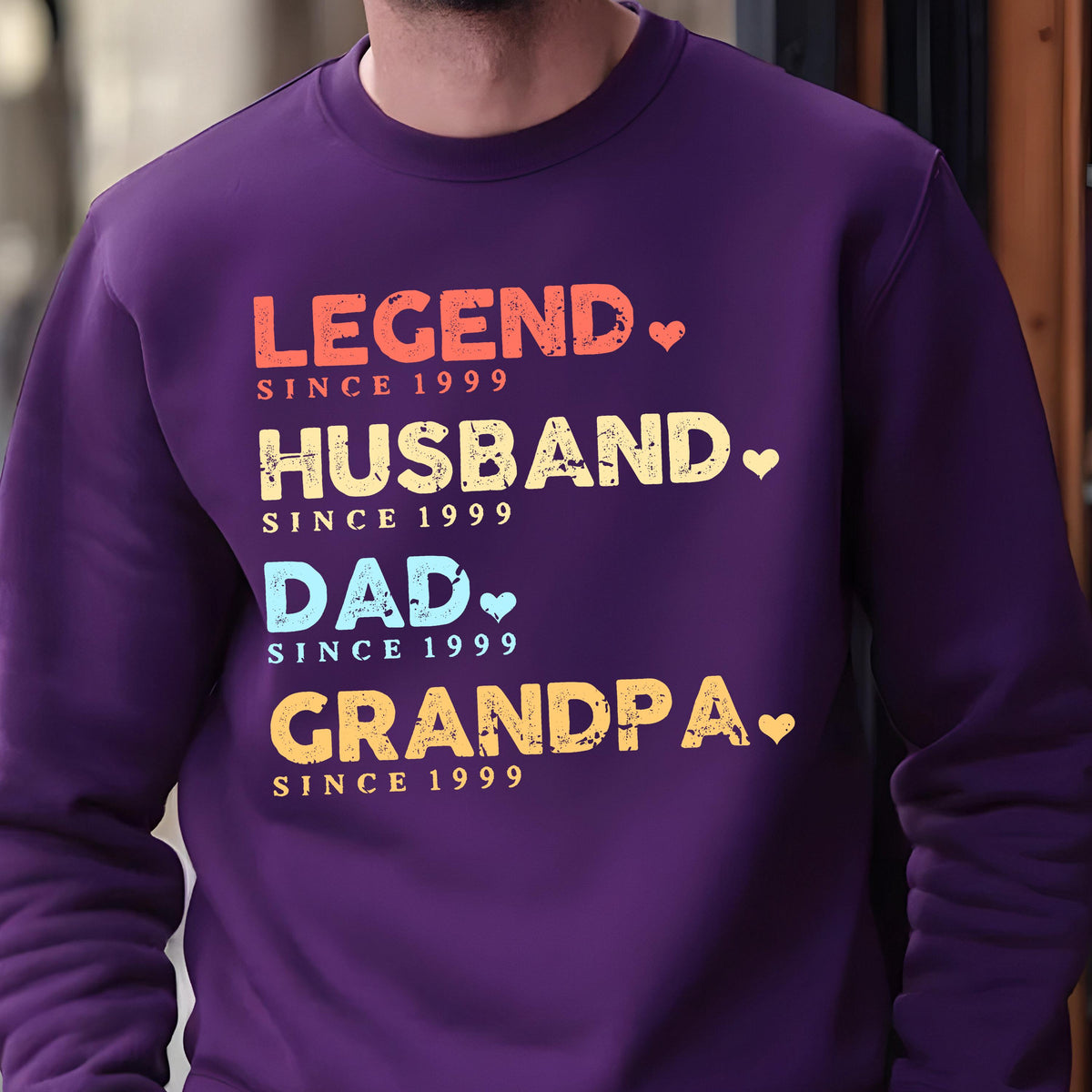 May include: A purple sweatshirt with the words "LEGEND," "HUSBAND," "DAD," and "GRANDPA" in various colors. Each word is followed by "SINCE 1999." The design includes small heart shapes.