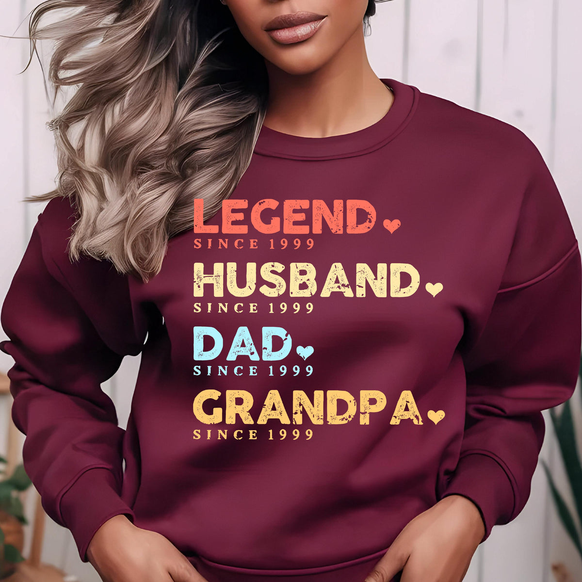 May include: Burgundy sweatshirt with the words "LEGEND, HUSBAND, DAD, GRANDPA" in colorful text, each with "SINCE 1999". The design includes small heart shapes. A casual top for a special person.