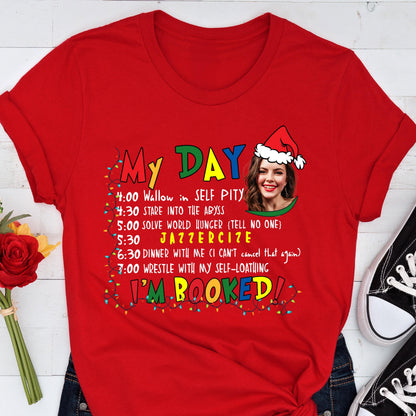May include: Red t-shirt with the text "My Day" and a humorous schedule including "Wallow in Self Pity" and "Jazzercise." A woman wearing a Santa hat is in the design. The words "I'm Booked!" are also on the shirt.
