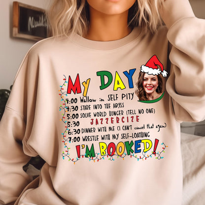 May include: A beige crewneck sweatshirt featuring a graphic print that reads MY DAY with a schedule including Wallow in self pity, Stare into the abyss, Solve world hunger, Jazzercise, Dinner with me, and Wrestle with my self-loathing, I'M BOOKED!