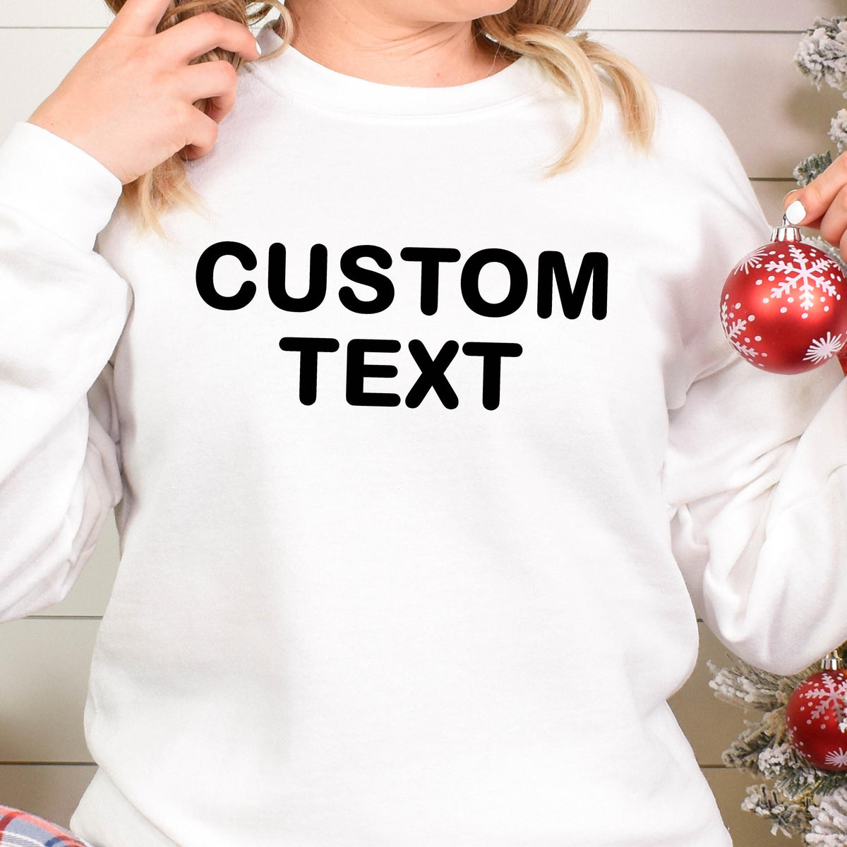 May include: A white long-sleeve crewneck sweatshirt featuring the words CUSTOM TEXT printed in bold black capital letters across the chest. The garment has a simple design with a ribbed neckline, cuffs, and hem, providing a clean look.