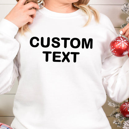 May include: A white long-sleeve crewneck sweatshirt featuring the words CUSTOM TEXT printed in bold black capital letters across the chest. The garment has a simple design with a ribbed neckline, cuffs, and hem, providing a clean look.