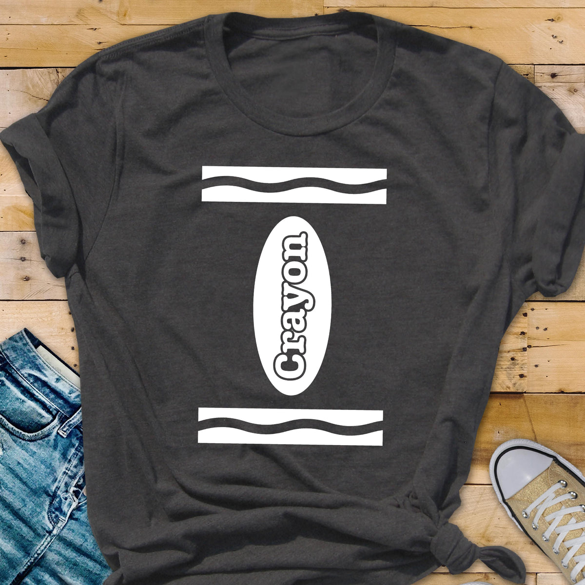 May include: A dark gray t-shirt with a white crayon design. The design features a white oval with the word "Crayon" written inside. The oval is surrounded by two white wavy lines.