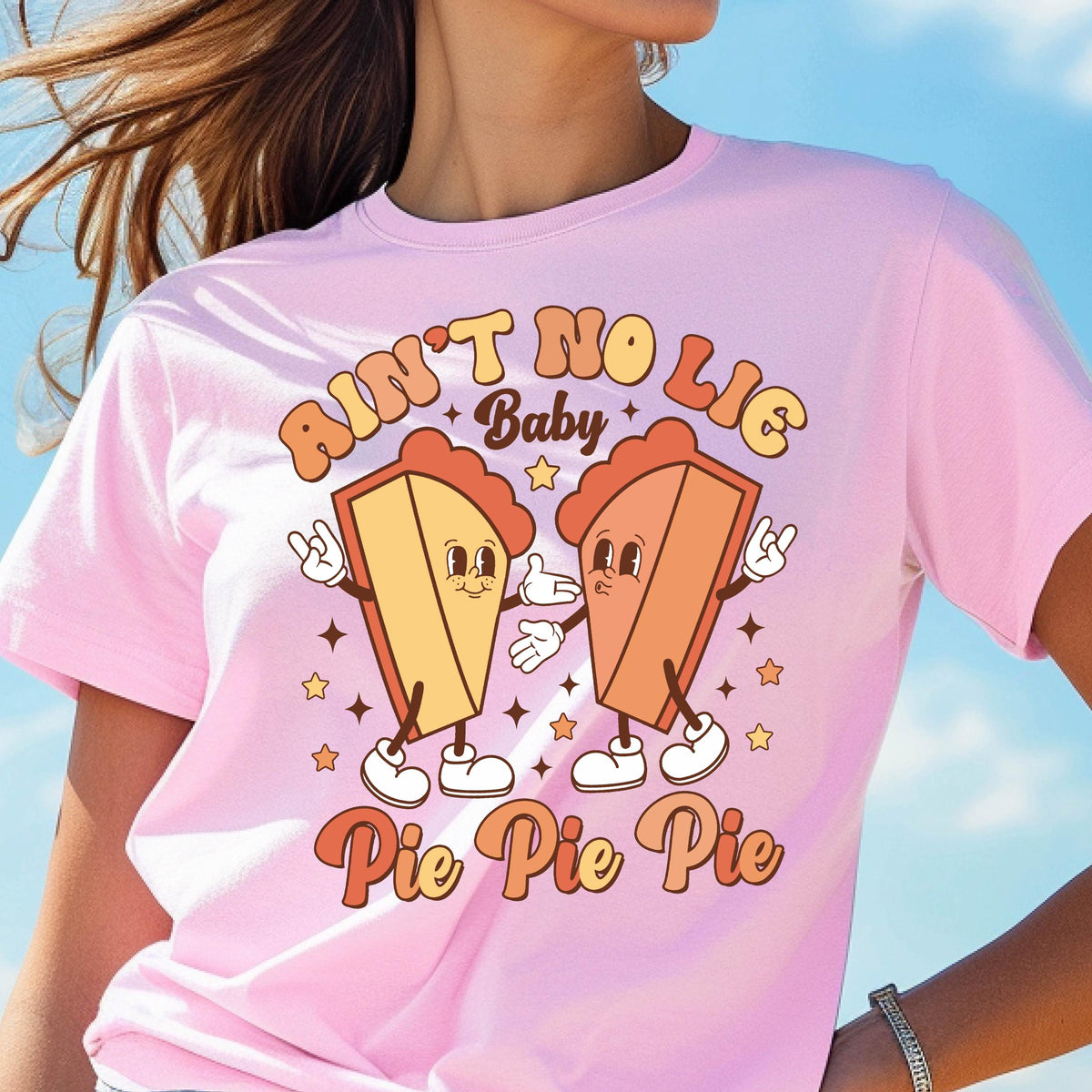 May include: Pink t-shirt with the text "Ain't No Lie Baby" and "Pie Pie Pie". The graphic features two cartoon pie slices with arms, legs, and faces. The pies are in shades of yellow and orange, with white shoes and star accents.