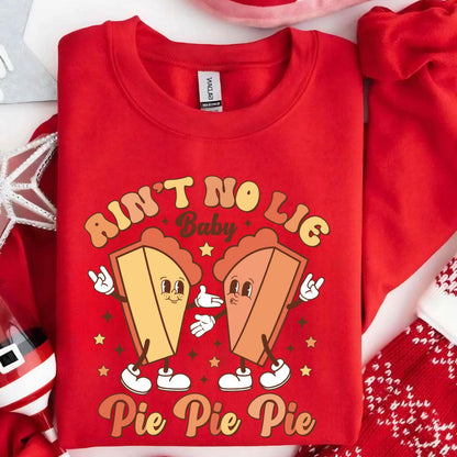 May include: A bright red crewneck sweatshirt featuring a graphic print of two cartoon pie slices with arms and legs. The text reads AIN'T NO LIE Baby Pie Pie Pie in a retro font. The pie characters are making hand gestures and wearing white shoes.