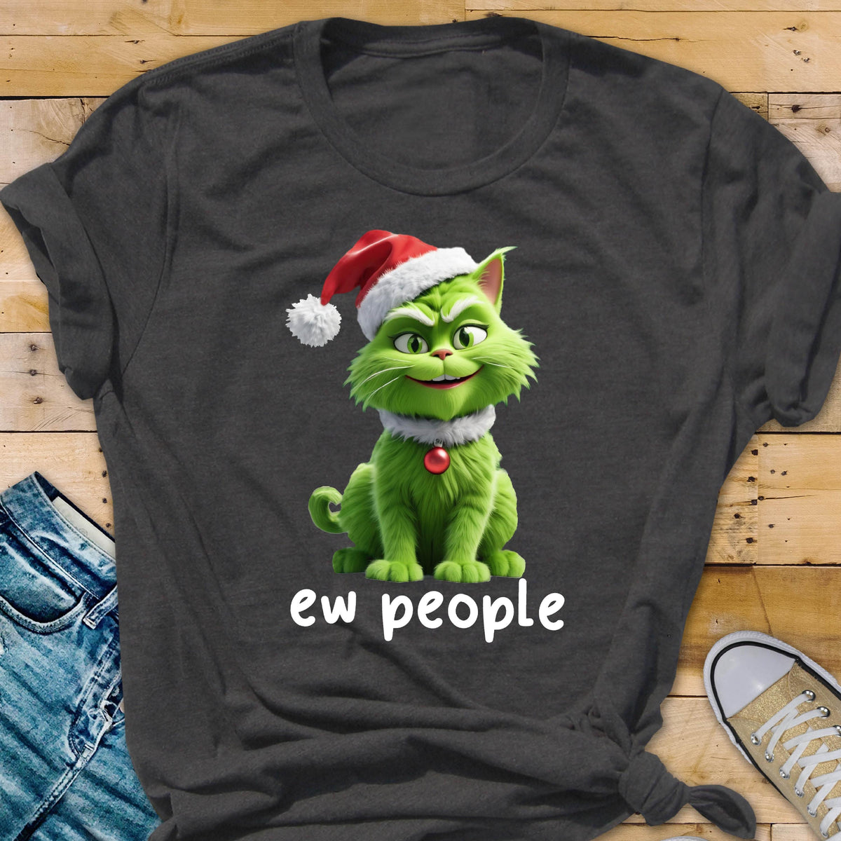 May include: A dark gray t-shirt featuring a graphic of a green cat wearing a red and white Santa hat and a red collar bell. The cat has a mischievous expression and is positioned above the white text that reads, "ew people" in lowercase.