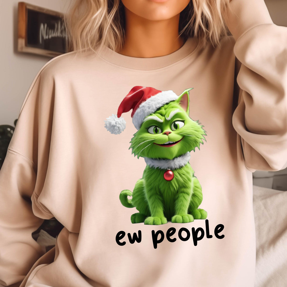 May include: Beige sweatshirt featuring a green cat character wearing a Santa hat and a collar with a red ornament. The text "ew people" is printed in black below the cat. The sweatshirt is a casual, festive garment.