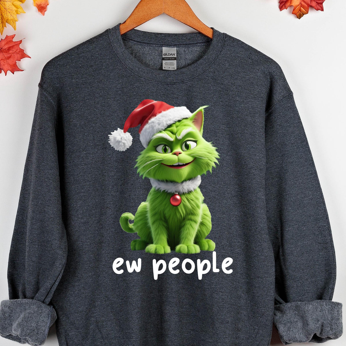 May include: Dark gray sweatshirt featuring a green cartoon cat wearing a Santa hat and a white collar with a red ornament. The text "ew people" is printed in white below the cat. The sweatshirt is hanging on a wooden hanger.
