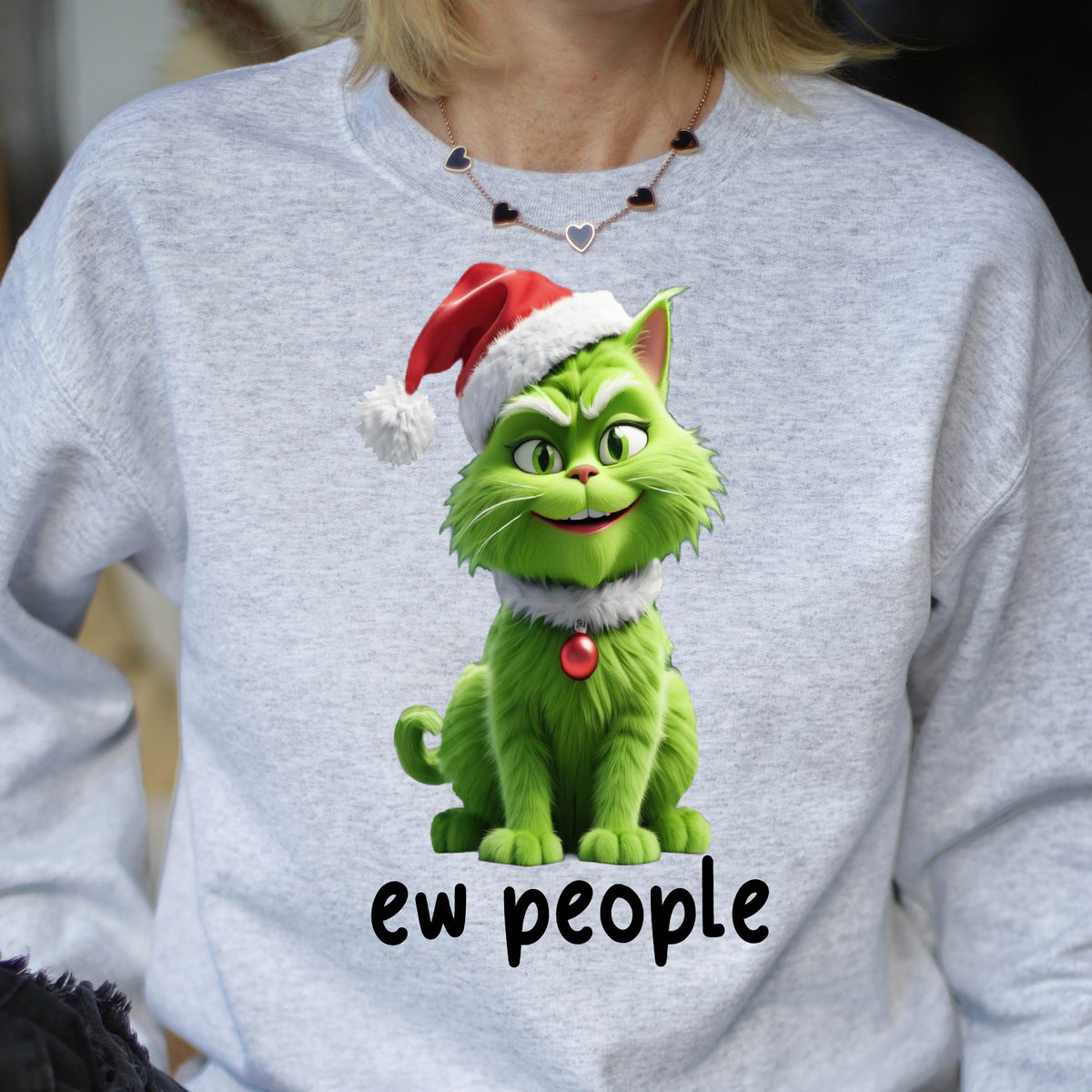 May include: A light gray sweatshirt featuring a green cartoon cat wearing a Santa hat and a white collar with a red ornament. The text "ew people" is printed in black below the cat.