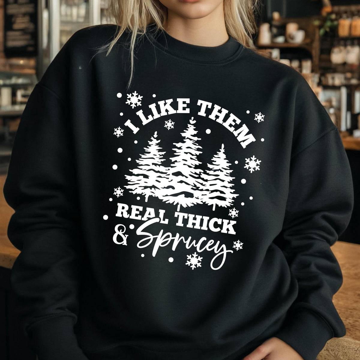 May include: A black crewneck sweatshirt featuring a white graphic print of three pine trees surrounded by snowflakes. The text reads I LIKE THEM REAL THICK & SPRUCEY in a combination of bold block lettering and a decorative script font style.