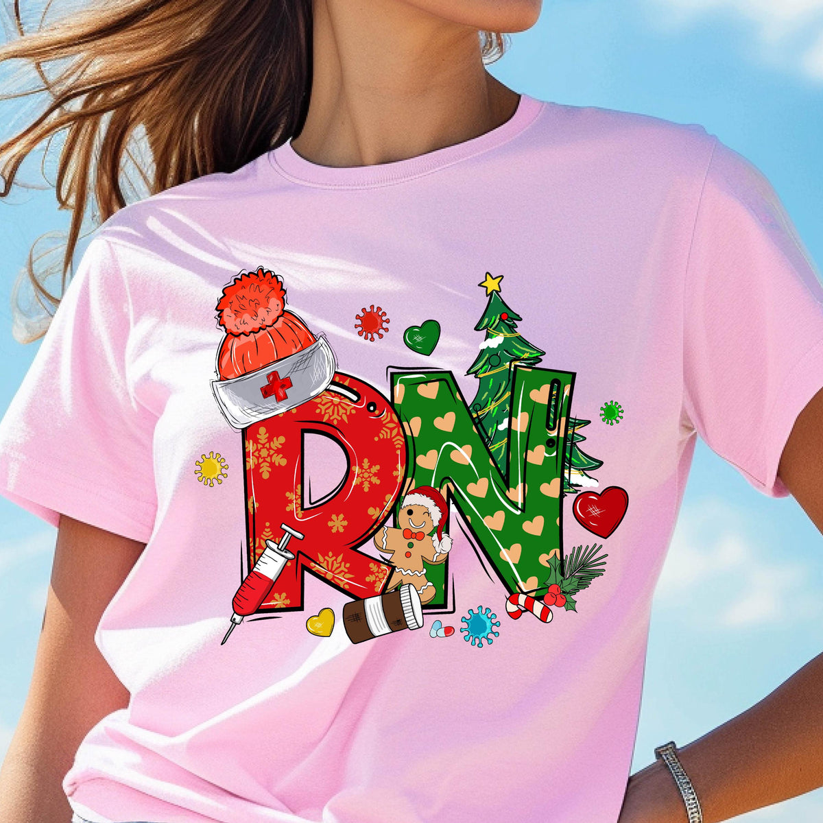 May include: Pink t-shirt with a festive RN design. The letters are decorated with Christmas-themed elements, including a Santa hat, snowflakes, a gingerbread man, and a Christmas tree. A syringe and pill bottle are also included in the design.