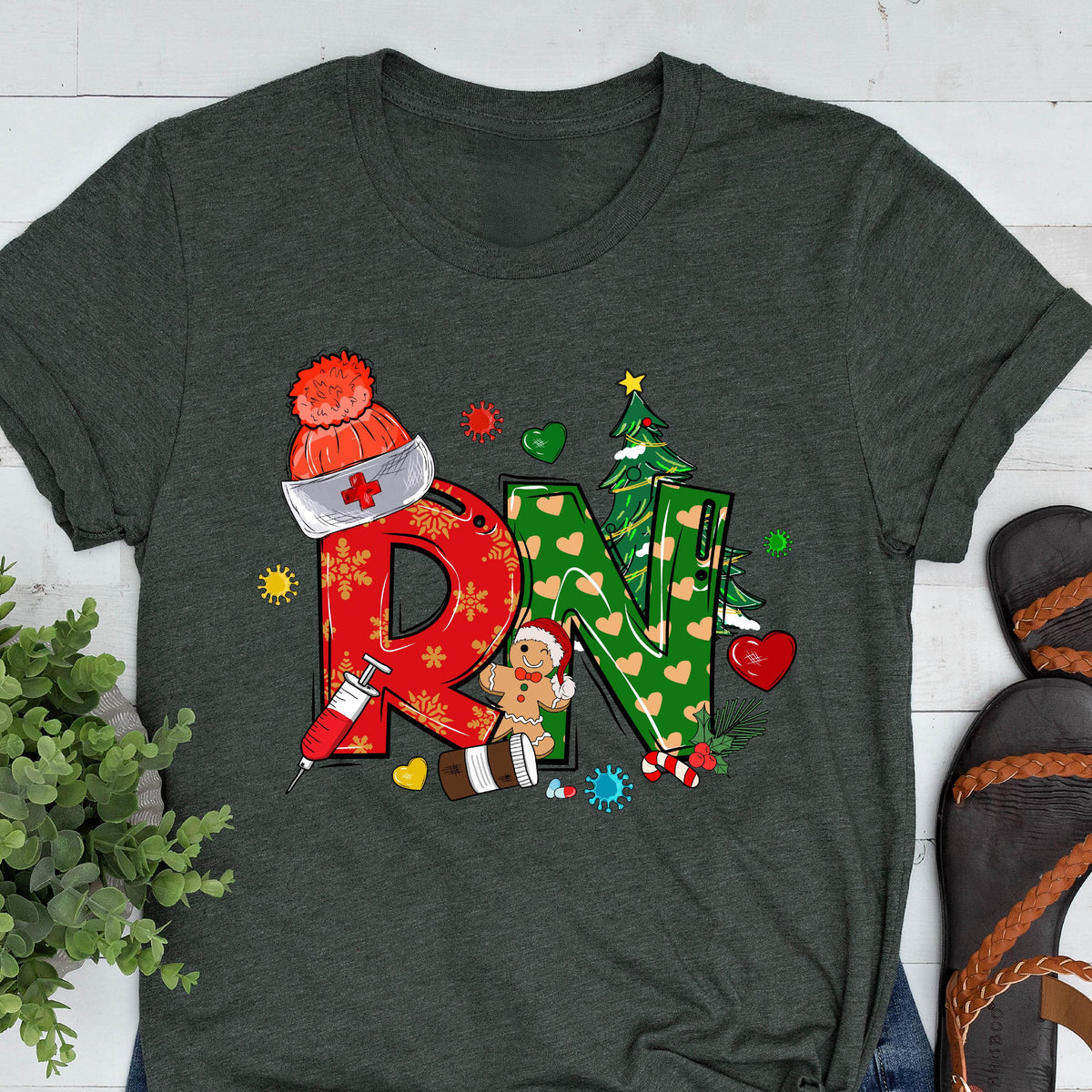 May include: Dark gray t-shirt featuring a festive design for a Registered Nurse. The design includes the letters "RN" in red and green, decorated with Christmas-themed elements like a Santa hat, gingerbread man, and Christmas tree.