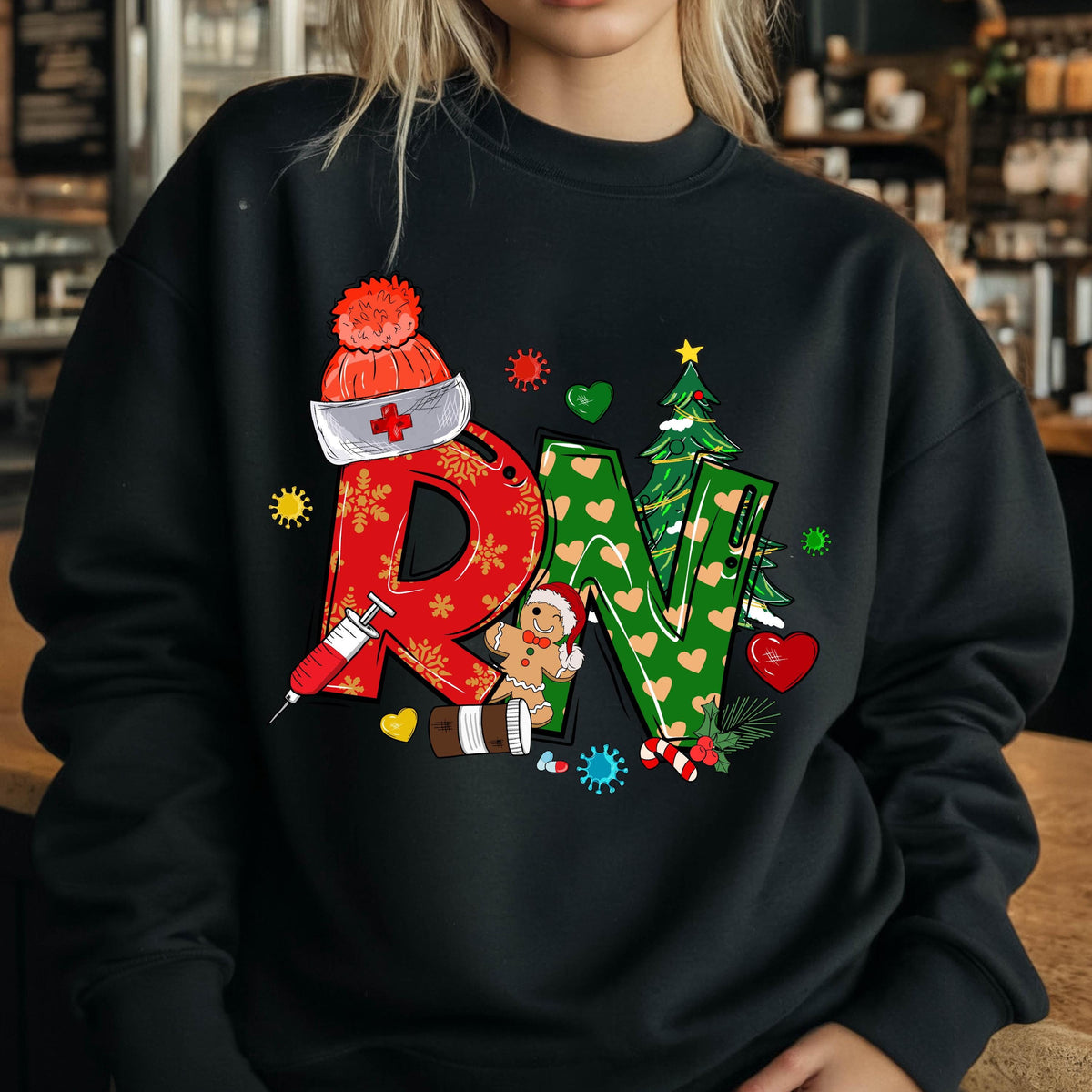 May include: A black crewneck sweatshirt featuring a graphic of the letters RN. The R is red with snowflakes, and the N is green with hearts. The design includes a nurse cap, a syringe, a gingerbread person, a Christmas tree, and medical icons.