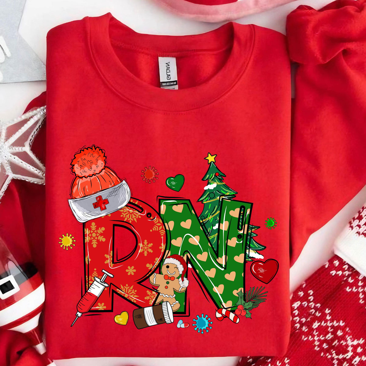 May include: A bright red crewneck sweatshirt featuring a large graphic with the letters RN in red and green. The design includes a nurse cap, a syringe, a gingerbread person, a Christmas tree, and various holiday-themed icons like hearts and snowflakes.