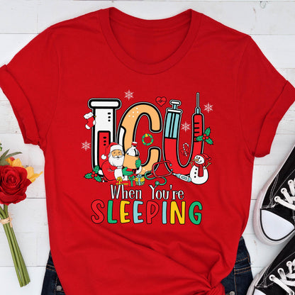 May include: A red t-shirt with a festive ICU design. The design includes the letters "ICU" in a medical theme, with Santa Claus, a snowman, and medical equipment. The text "When You're Sleeping" is below the ICU letters.